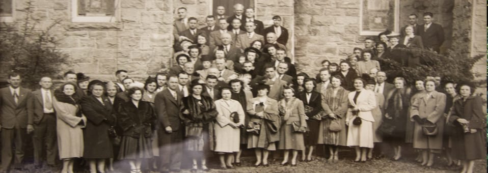 Fotografía histórica de una congregación temprana de First Christian Church Anniston reunida afuera de un edificio de piedra